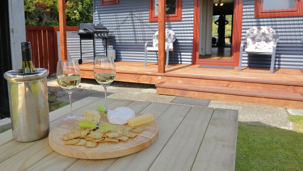 Een terras met een houten tafel, een fles wijn, glazen, kaas en koekjes.