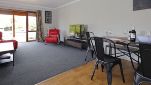 Een moderne woonkamer met een rode fauteuil, een eettafel met stoelen, een televisie en een fles wijn.