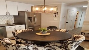 Une cuisine moderne avec des meubles blancs, des appareils en acier inoxydable et une table de salle à manger ronde, assortie de chaises en cuir.