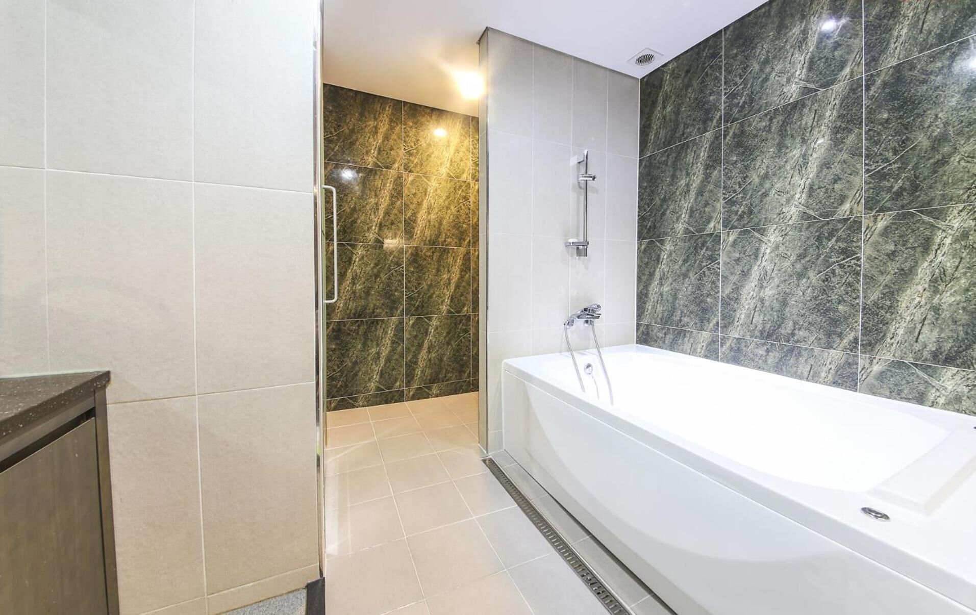 A modern bathroom with a large bathtub, a shower area, and marble walls.