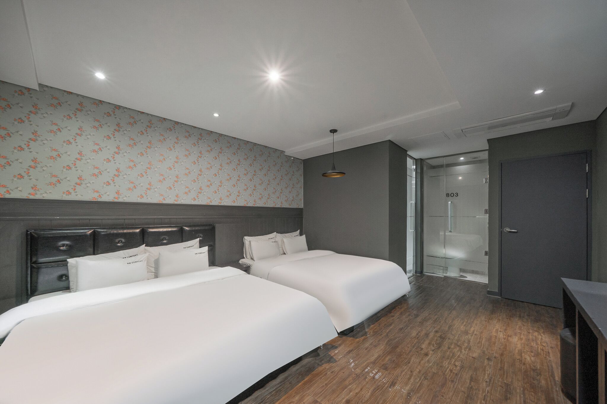Ein Hotelzimmer mit zwei Betten, Holzboden, floralem Wandpapier und modernem Design.