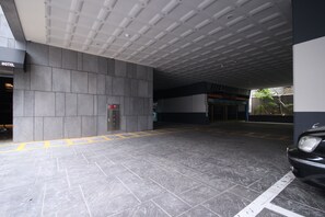 Entrada de hotel con piso de baldosas, un ascensor a la vista y un coche aparcado a la derecha.