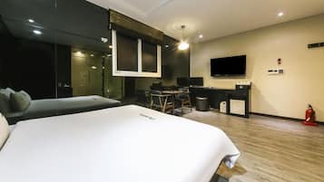 Habitación de hotel con una cama grande, un escritorio con una computadora, un televisor y una pequeña zona de estar.