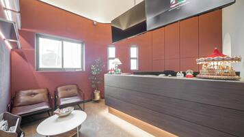 A reception area with a modern design, featuring a dark wood reception desk, leather chairs, a small table with a bowl, and a decorative carousel.