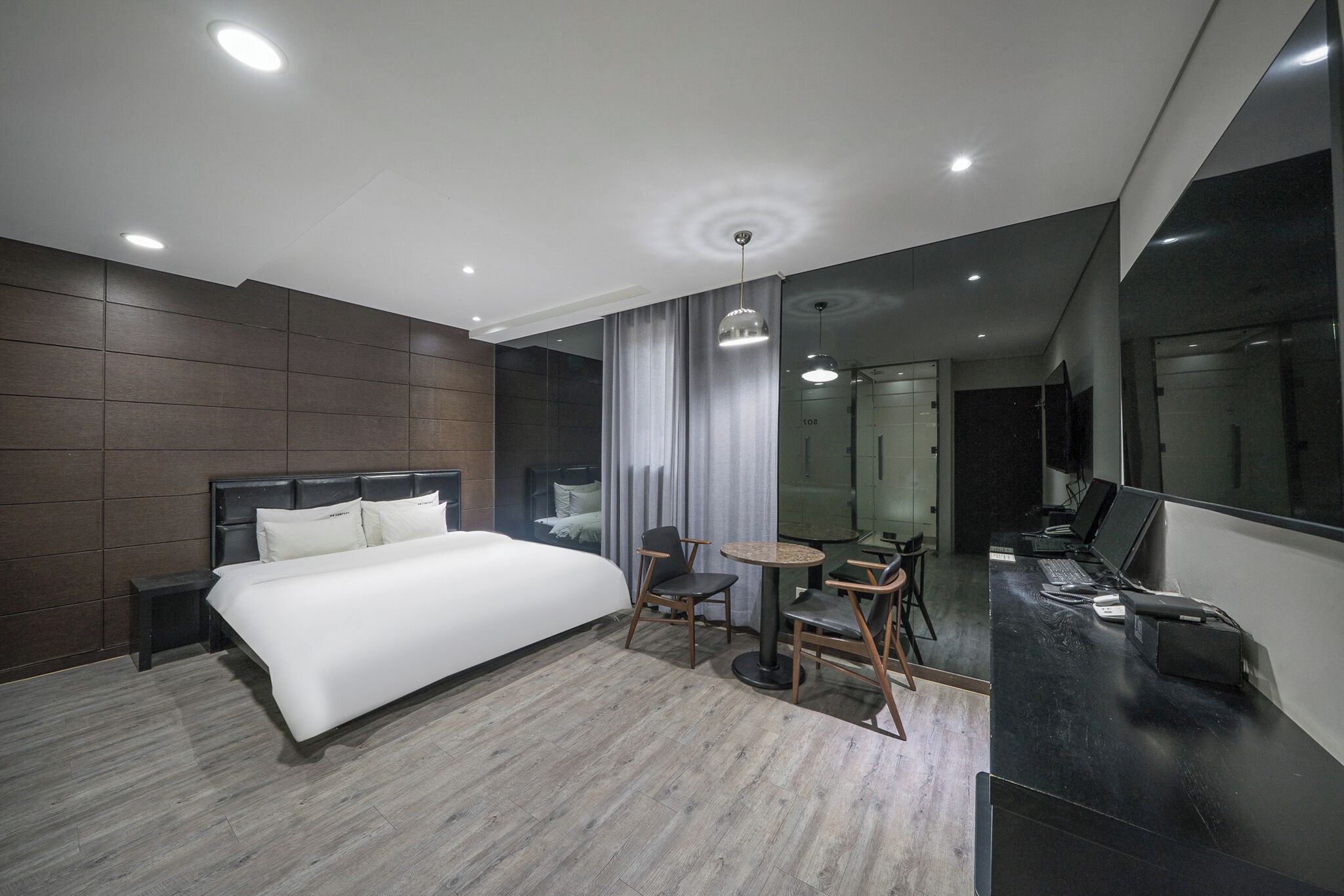 A modern hotel room with a large bed, a desk with a computer, a chair, and a small table.