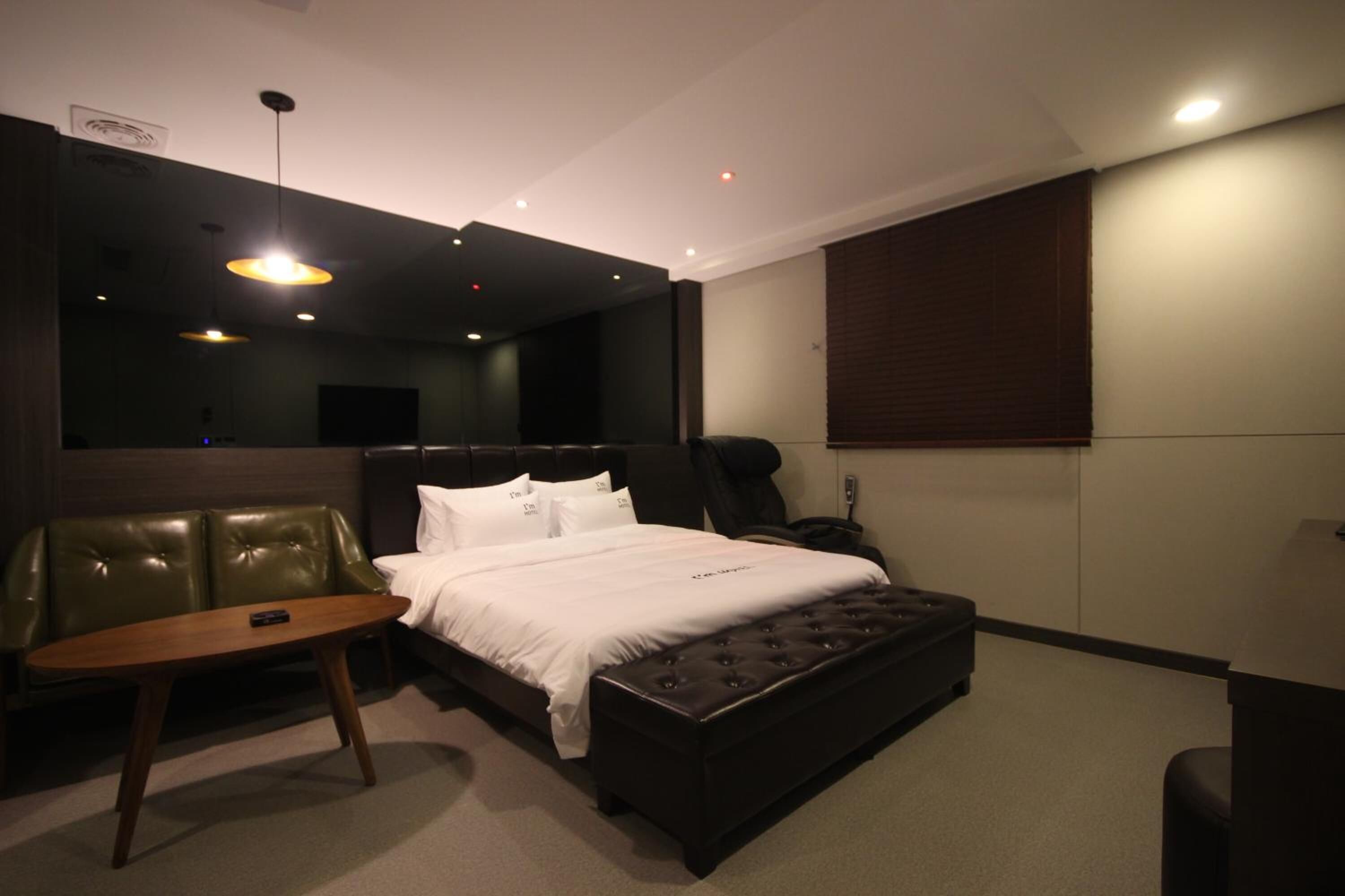 A modern hotel room with a large bed, a leather sofa, a small wooden table, and a large mirror.