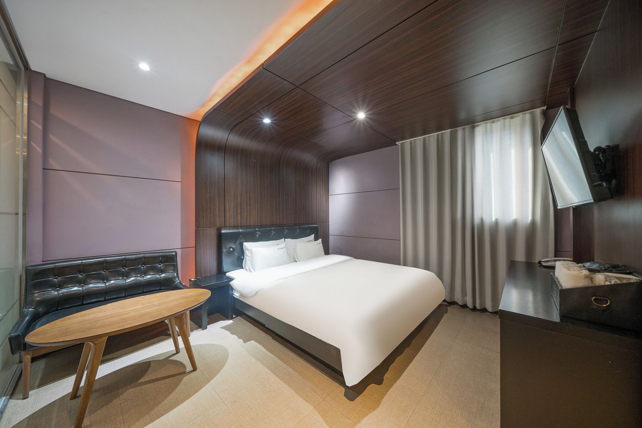 A modern hotel room with a bed, a seating area, a desk, and a television.