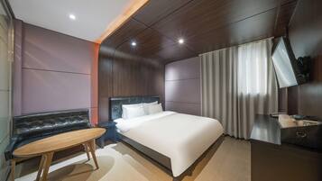 A modern hotel room with a bed, a seating area, a desk, and a television.