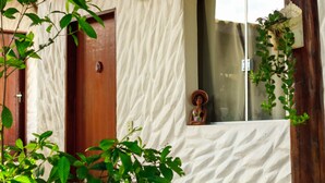A building with a textured facade, a wooden door, a window with a decorative figure, and a hanging plant. - Pousada Jardim da Nova Era (Alto Paraíso de Goiás)