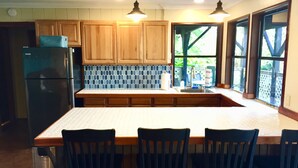 A kitchen with wooden cabinets, a stainless steel refrigerator, a tiled backsplash, and a large island with bar stools. - 2 Bedroom Kona Coffee Farm with Ocean Views in Holualoa (Holualoa)