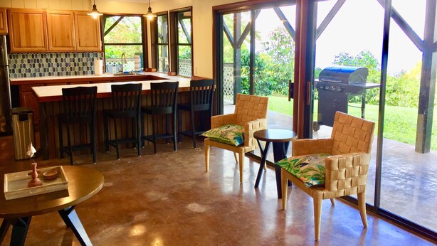A kitchen with wooden cabinets, a bar area, and a dining space with chairs and a table. - 2 Bedroom Kona Coffee Farm with Ocean Views in Holualoa (Holualoa)