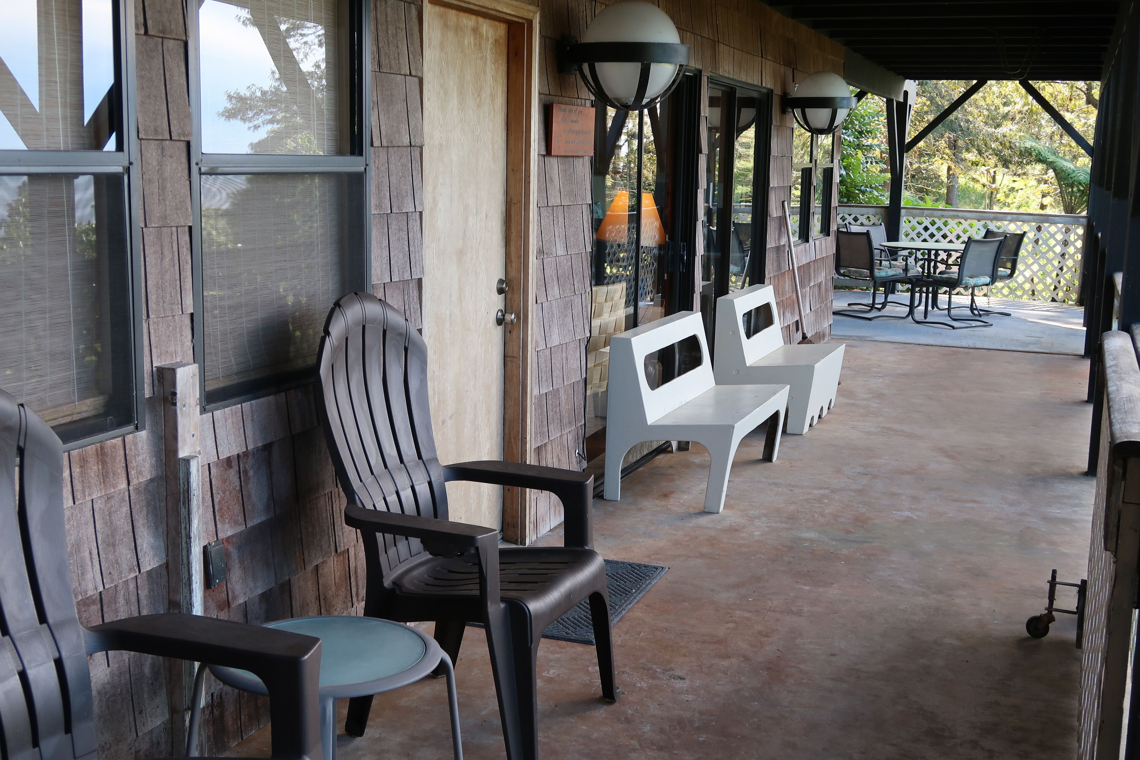 Un espace extérieur abrité, aménagé avec des chaises et des tables, doté de murs en bois et offrant une vue sur les arbres environnants.