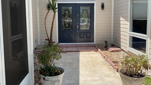A house entrance with a dark blue door, a small garden with potted plants, and a concrete pathway leading to the door. - Steps to the ocean and inlet (Hutchinson Island)