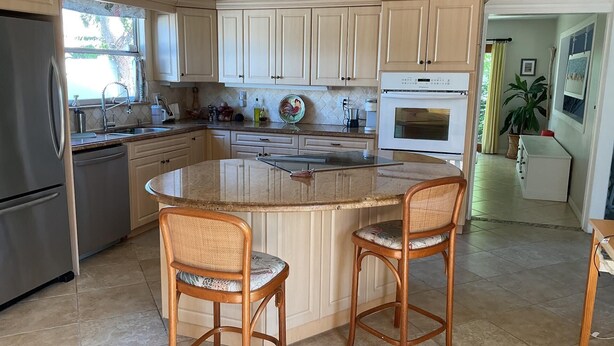 A kitchen with a central island, two bar stools, a refrigerator, a dishwasher, and a microwave. - Steps to the ocean and inlet (Hutchinson Island)