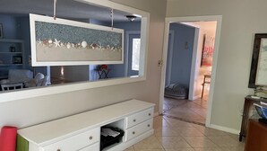 A living room with a large wall-mounted TV, a white entertainment unit, and a hallway leading to another room. - Steps to the ocean and inlet (Hutchinson Island)
