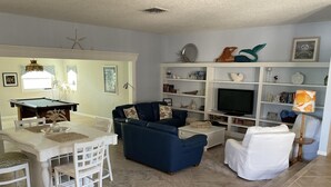 A living room with a pool table, a blue sofa, a white armchair, and a TV on a white stand. - Steps to the ocean and inlet (Hutchinson Island)