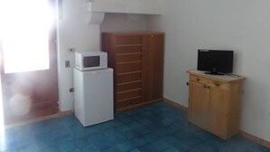 Ein kleiner Raum mit einem weißen Kühlschrank, einer Mikrowelle, einem Holzschrank und einem Fernseher.