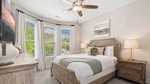 A bedroom with a bed, bedside lamps, a nightstand, a ceiling fan, and a large window with curtains. - Wright Place - Walk to Downtown - 0.5 mi to UofA (Fayetteville)