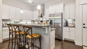 A modern kitchen with white cabinetry, a stainless steel refrigerator, a bar area with stools, and a hanging light fixture. - Wright Place - Walk to Downtown - 0.5 mi to UofA (Fayetteville)