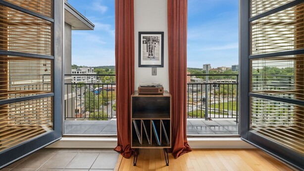 A balcony with a view of the city, a framed picture on the wall, and a small shelf with items. - The Axis - Condo on Dickson St - Walk to UofA (Fayetteville)