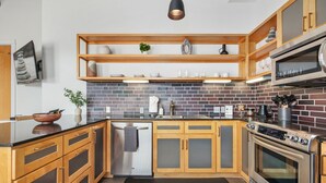 A modern kitchen with wooden cabinets, a brick backsplash, stainless steel appliances, and built-in shelves. - The Axis - Condo on Dickson St - Walk to UofA (Fayetteville)