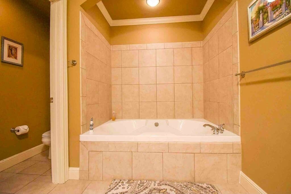 A bathroom with a large bathtub, tiled walls, a toilet, and a patterned rug.