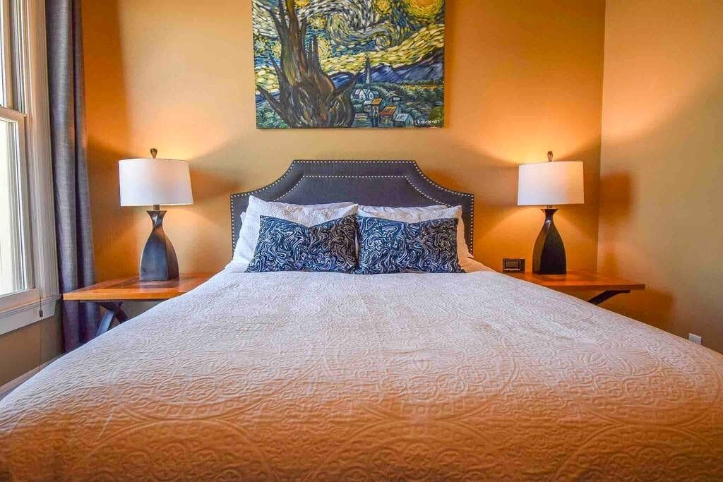 Une chambre d’hôtel avec un grand lit, deux tables de chevet avec des lampes, un tableau au mur et une fenêtre avec des rideaux.
