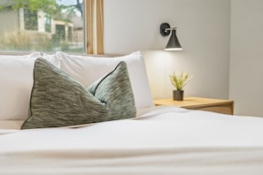 A bed with white bedding, a green textured pillow, a bedside lamp, and a small potted plant on a wooden nightstand. - Overlook - Hot Tub - Beaver Lake (Garfield)