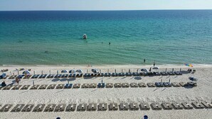 A beach with rows of sun loungers and umbrellas, a clear blue sea, and a few people in the water. - Tidewater by Forehand Rentals (Panama City Beach)