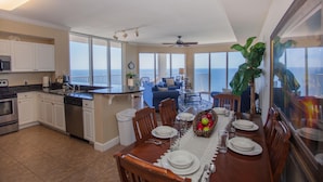A spacious kitchen with white cabinets, a dishwasher, and a dining area with a table set for four. - Tidewater by Forehand Rentals (Panama City Beach)