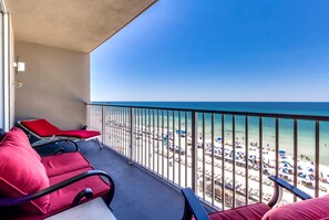 A balcony with red chairs and a table, overlooking a beach with umbrellas and people. - Tidewater by Forehand Rentals (Panama City Beach)