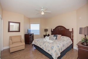 A bedroom with a large bed, a chair, a desk, and a ceiling fan. - Tidewater by Forehand Rentals (Panama City Beach)