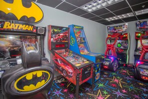 Ein Raum mit Spielautomaten, darunter ein Batman-Automaten, ein Rennspiel und ein farbenfroher Boden mit Sternenmustern.