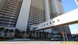 A high-rise hotel with multiple floors, a covered walkway, and palm trees in the foreground. - Tidewater by Forehand Rentals (Panama City Beach)