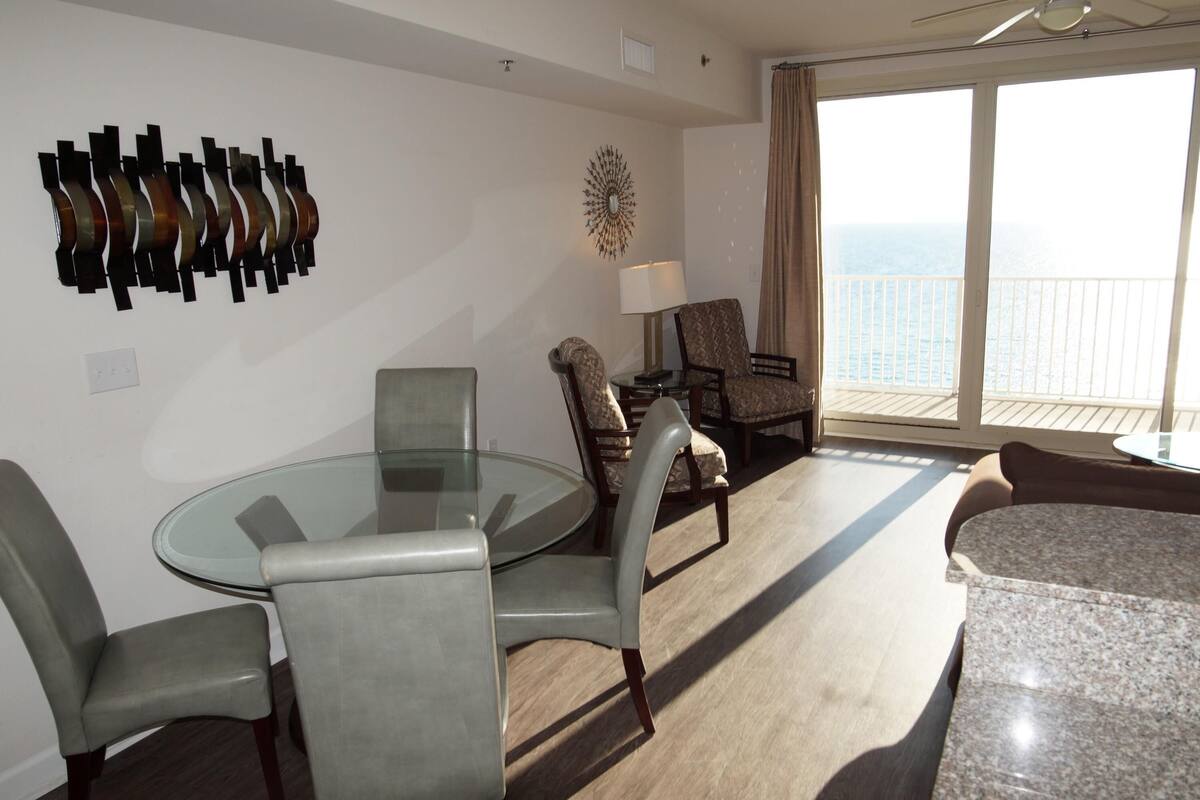 A modern living room with a glass table, two armchairs, a sofa, a lamp, and a decorative wall piece.
