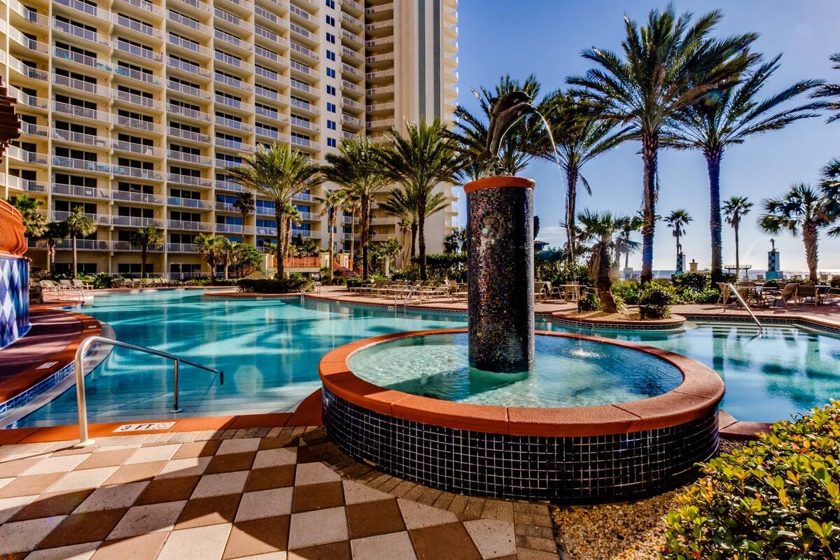 A hotel pool area with a hot tub, palm trees, and a tall building in the background.