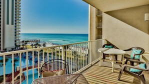 A balcony with a view of the ocean, a pool, and a dining area with chairs and a table. - Shores of Panama by Forehand Rentals (Panama City Beach)