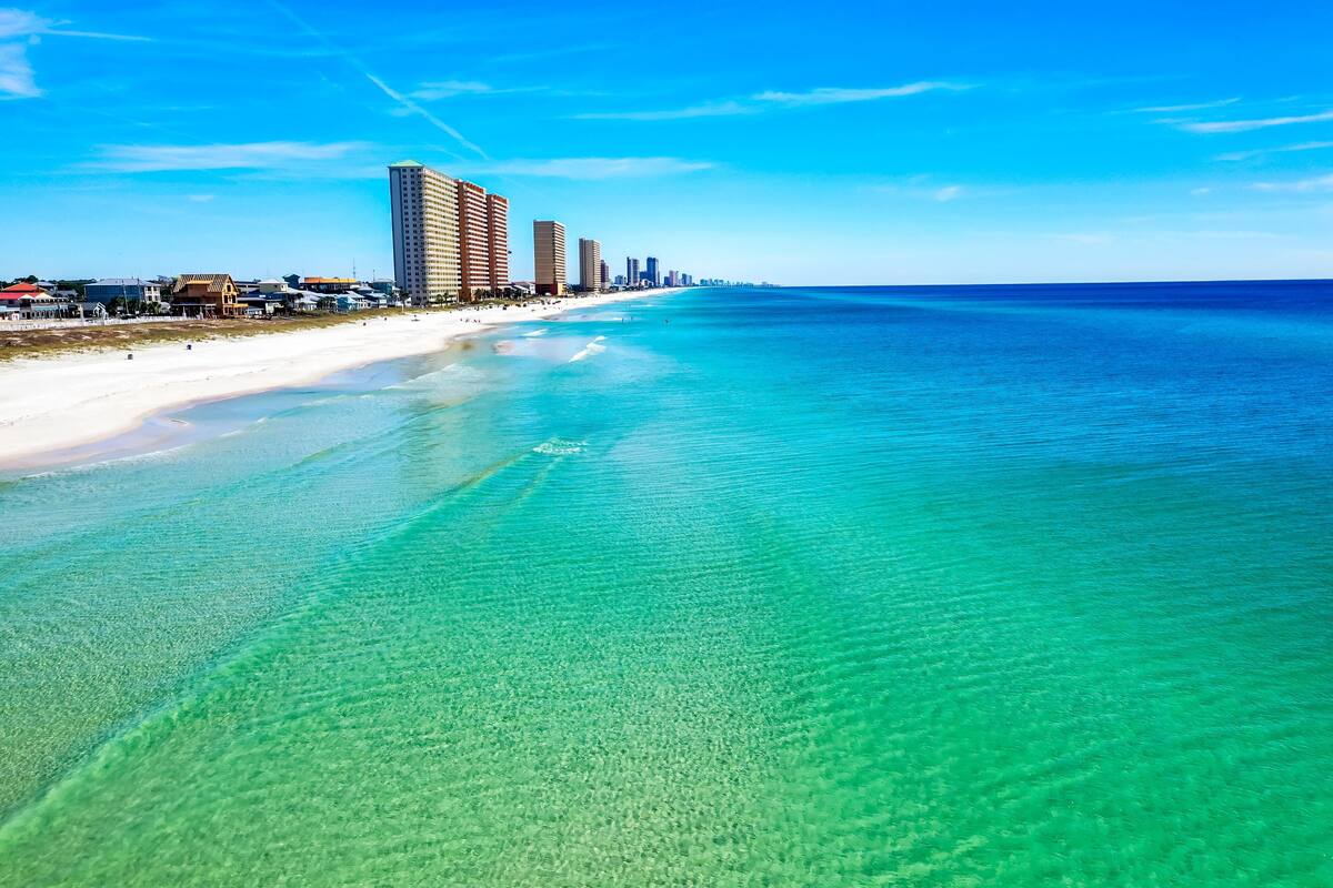 Un paisaje costero con playa, aguas turquesas cristalinas y altos edificios a lo largo de la orilla.
