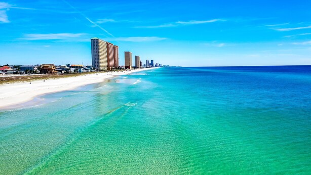 Un paisaje costero con playa, aguas turquesas cristalinas y altos edificios a lo largo de la orilla.