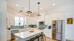 Una cocina moderna con armarios blancos, electrodomésticos de acero inoxidable y una isla central con taburetes.