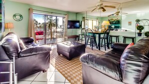 A living room with a sofa, ottoman, and a dining area with a table and chairs. - The Summit by Forehand Rentals (Panama City Beach)
