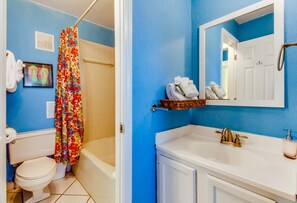 A bathroom with a blue wall, white toilet, shower curtain, and a sink with a mirror above it. - The Summit by Forehand Rentals (Panama City Beach)