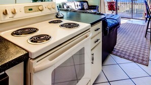 A compact kitchen with a stove, oven, and a dining area with a table and chairs. - The Summit by Forehand Rentals (Panama City Beach)