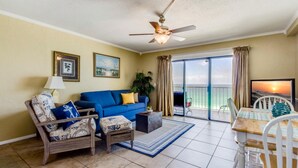 A living room with a blue sofa, a wooden armchair, a coffee table, and a dining area with a table and chairs. - The Summit by Forehand Rentals (Panama City Beach)