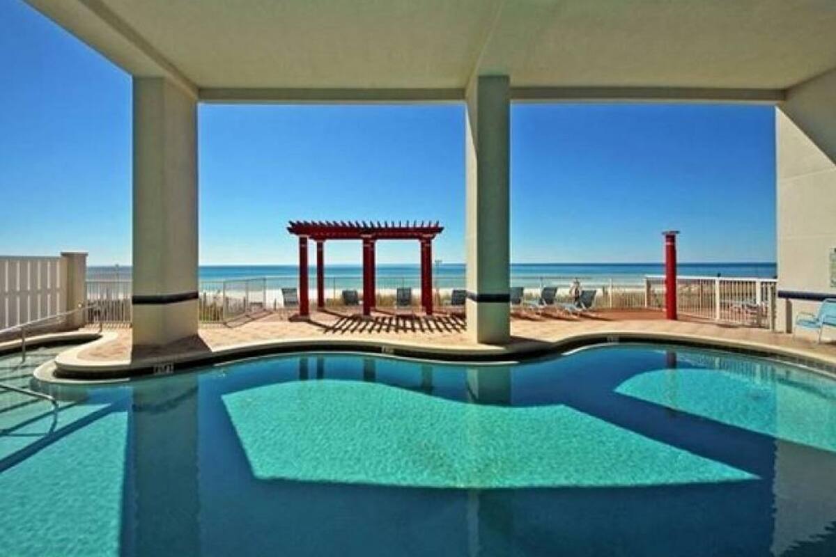 Un área de piscina con vistas a la playa, una pérgola roja y sillones de descanso.