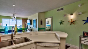A kitchen with a dishwasher, a sink, and a window overlooking the sea. - Celadon: Unit 102 by Forehand Rentals (Panama City Beach)