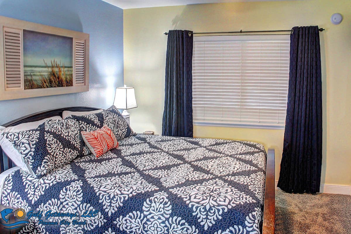 A bedroom with a bed, a nightstand, a lamp, and a window with curtains.
