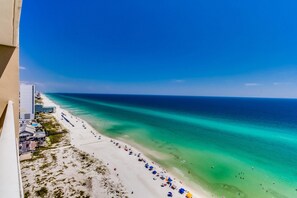 Une plage offrant une vue magnifique, avec une longue étendue de sable blanc, une eau turquoise cristalline et une rangée de parasols colorés le long du rivage.