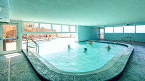 En indendørs swimmingpool med krystalklart, blåt vand, omgivet af vinduer og flisegulv.