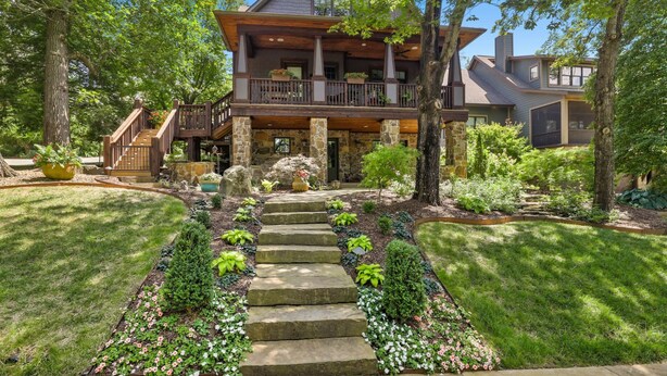 Una casa de dos pisos con fachada de piedra, una terraza de madera y una escalera de piedra que conduce a la entrada.
